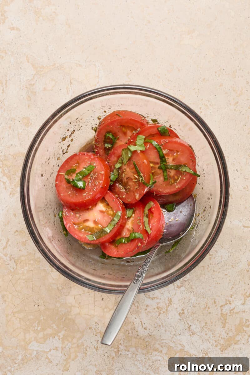 Sliced tomatoes and basil leaves soaking in a balsamic and olive oil mixture in a bowl.