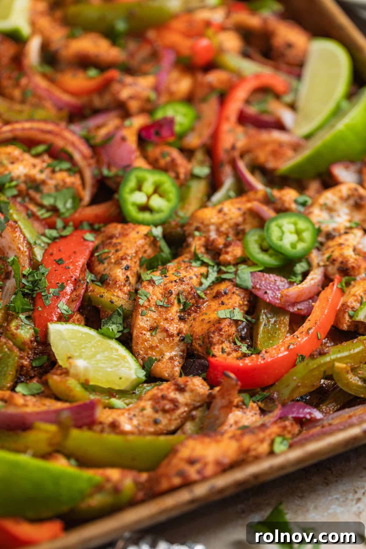 Sheet pan with baked honey lime chicken fajitas with red onion, bell peppers and topped with chopped cilantro.