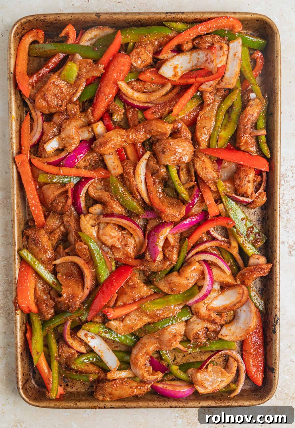Raw sliced chicken, peppers and onion seasoned and spread on sheet pan.
