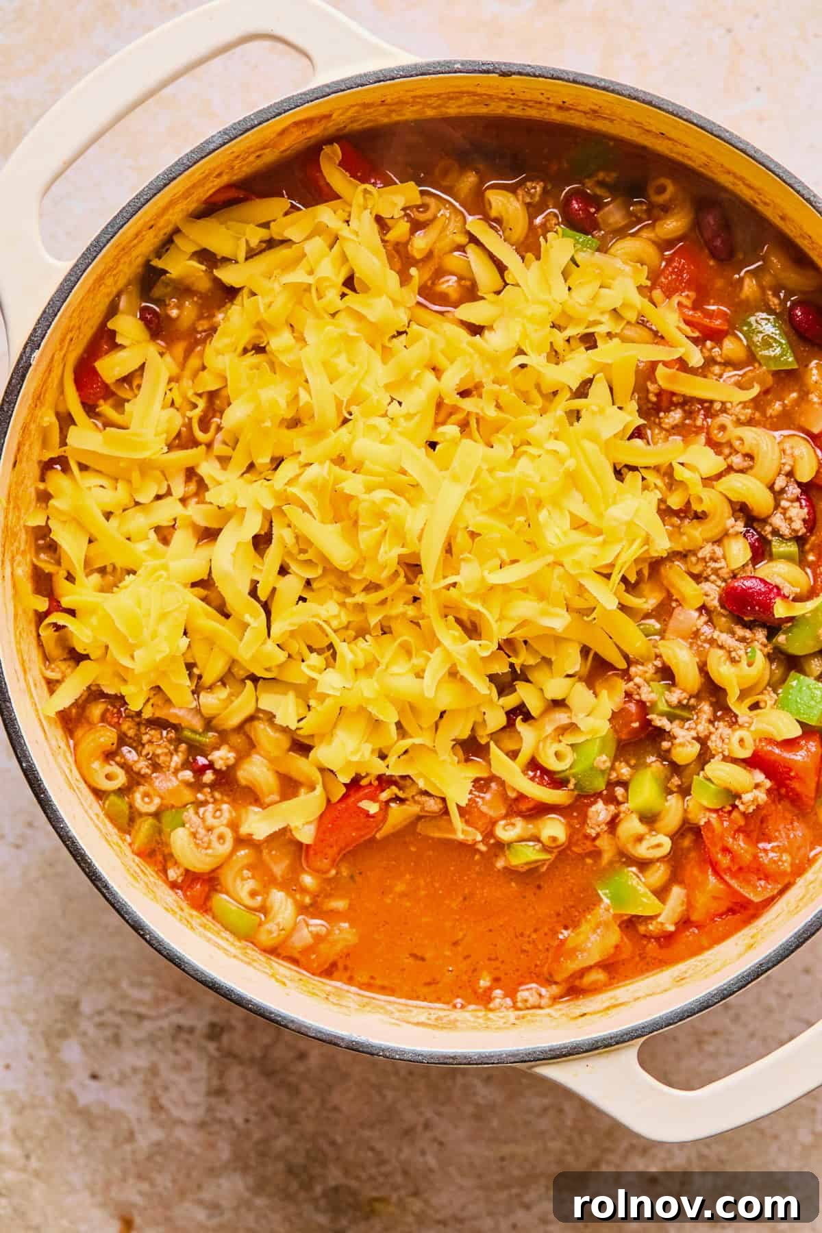 Hearty Skillet Chili Mac 11 Shredded cheddar cheese being stirred into the hot chili and macaroni mixture until fully melted and creamy.