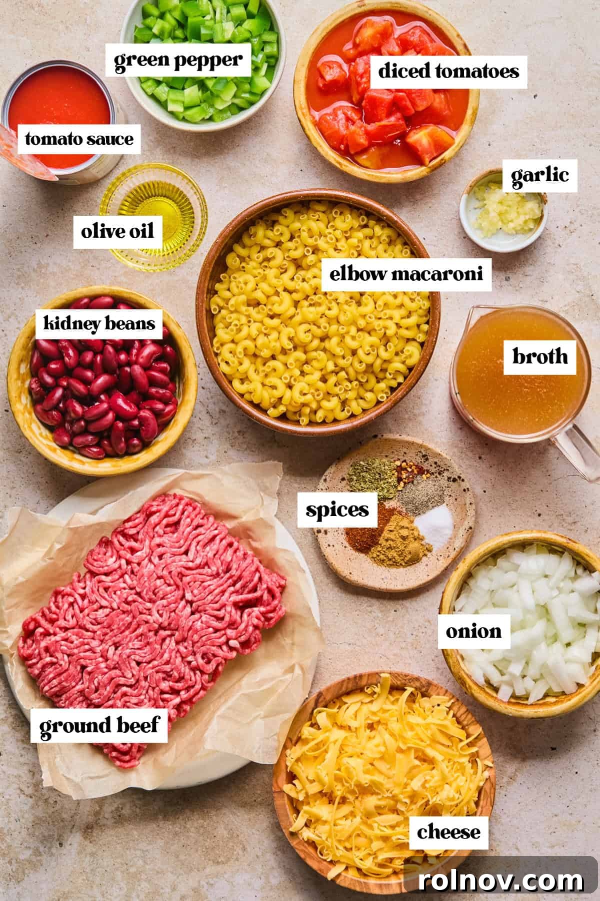 Hearty Skillet Chili Mac 4 A curated selection of fresh ingredients laid out on a kitchen counter, including ground beef, bell peppers, various cheeses, uncooked pasta, beans, and spices, ready for making chili mac.