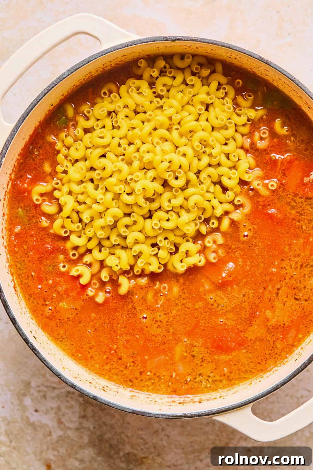 Hearty Skillet Chili Mac 10 Uncooked elbow macaroni pasta being stirred into the simmering chili mixture in the pot.