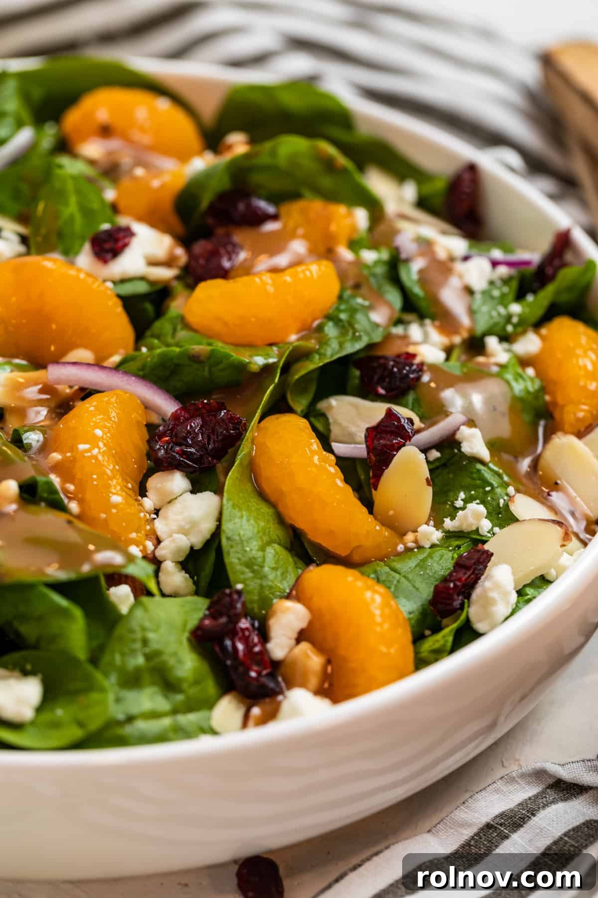 Sunshine Spinach Salad with Honey Balsamic 2 White bowl with spinach mandarin salad topped with goat cheese, cranberries, toasted almonds, and a drizzle of honey balsamic dressing. The colors are vibrant and inviting.