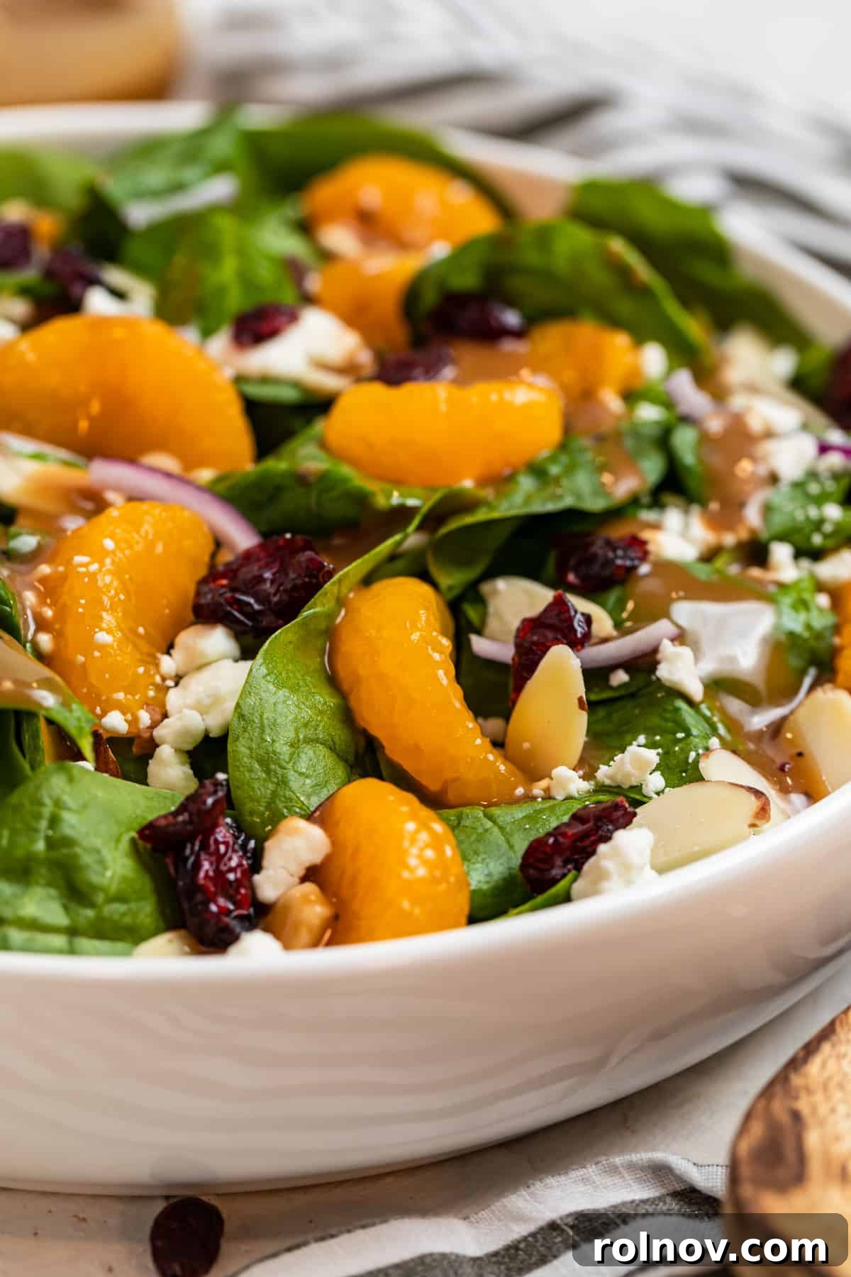 Sunshine Spinach Salad with Honey Balsamic 4 White bowl with a vibrant spinach, mandarin orange, and almond salad, accompanied by a wooden spoon on a rustic wooden surface, highlighting its natural freshness.