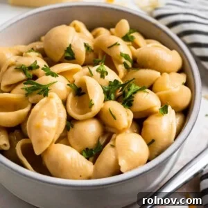 Foolproof Instant Pot Mac and Cheese 7 Creamy macaroni and cheese shells in a rustic clay bowl, garnished with fresh chopped parsley.