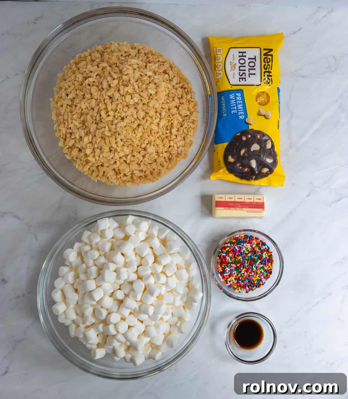 Festive Sprinkled Krispie Treats 3 A vibrant display of ingredients for Funfetti Rice Krispie Treats: cereal, marshmallows, colorful sprinkles, and white chocolate chips neatly arranged on a kitchen counter.