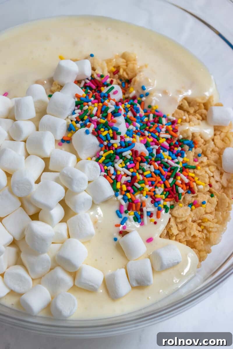 Festive Sprinkled Krispie Treats 4 A large mixing bowl filled with rice cereal, a mound of mini marshmallows, and a generous amount of colorful rainbow sprinkles, ready to be combined.