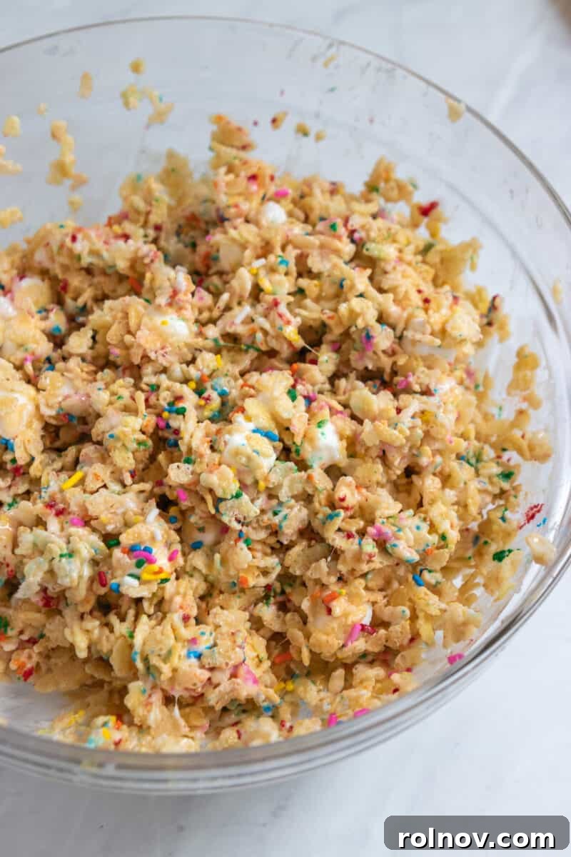 Festive Sprinkled Krispie Treats 5 Close-up of a mixing bowl containing the funfetti rice krispie treat mixture, showcasing the melted marshmallow coating the cereal and sprinkles.