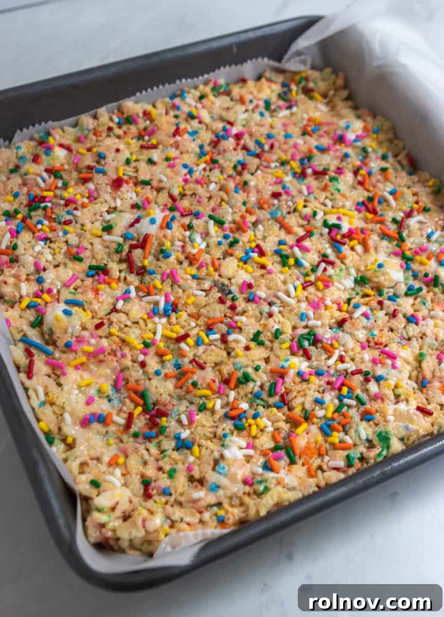 Festive Sprinkled Krispie Treats 6 A baking pan filled with freshly pressed Funfetti Rice Krispie Treats, adorned with a final layer of colorful rainbow sprinkles on top.