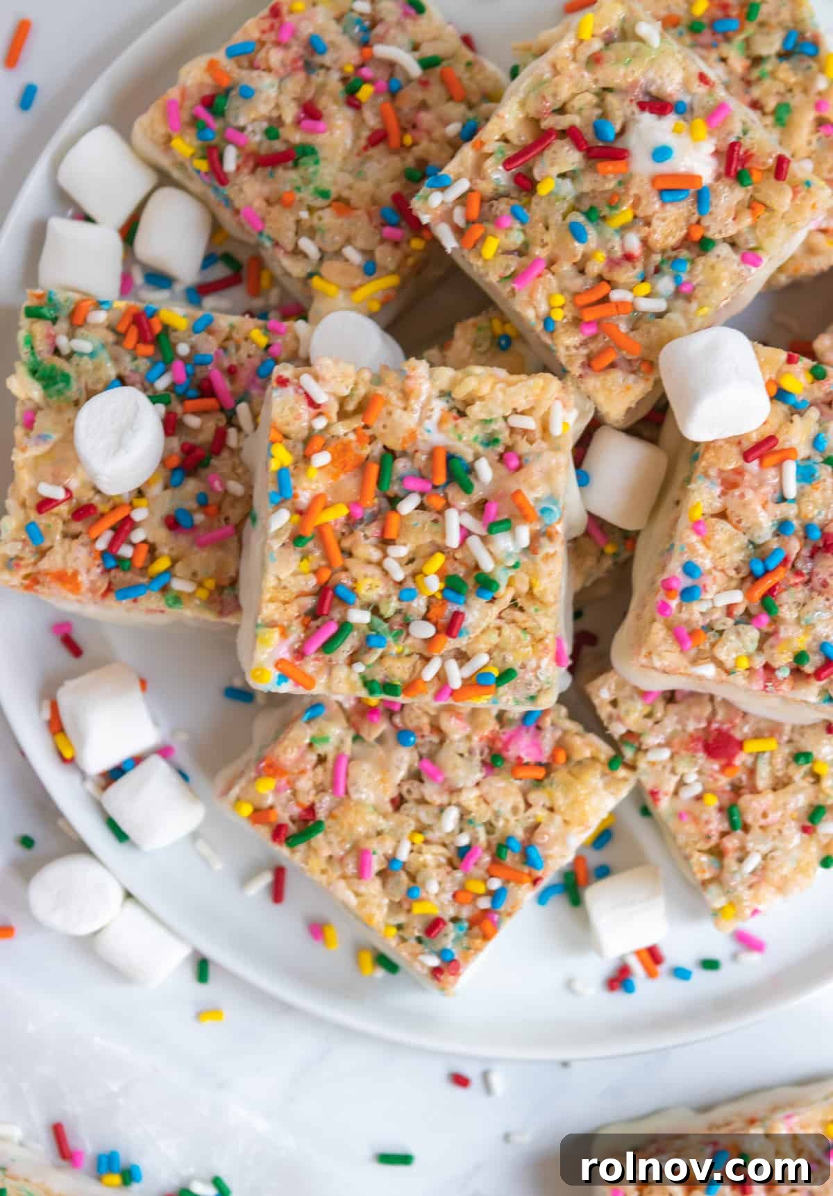Festive Sprinkled Krispie Treats 8 An overhead view of beautifully arranged Funfetti Rice Krispie Treats on a plate, surrounded by loose sprinkles and extra mini marshmallows, highlighting their colorful appeal.