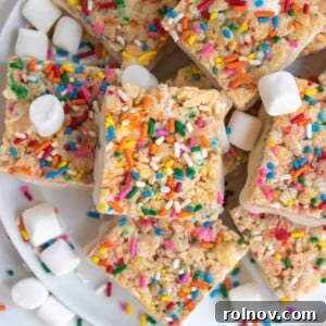 Festive Sprinkled Krispie Treats 9 Overhead view of birthday cake rice krispie treats on white plate with sprinkles and marshmallows.
