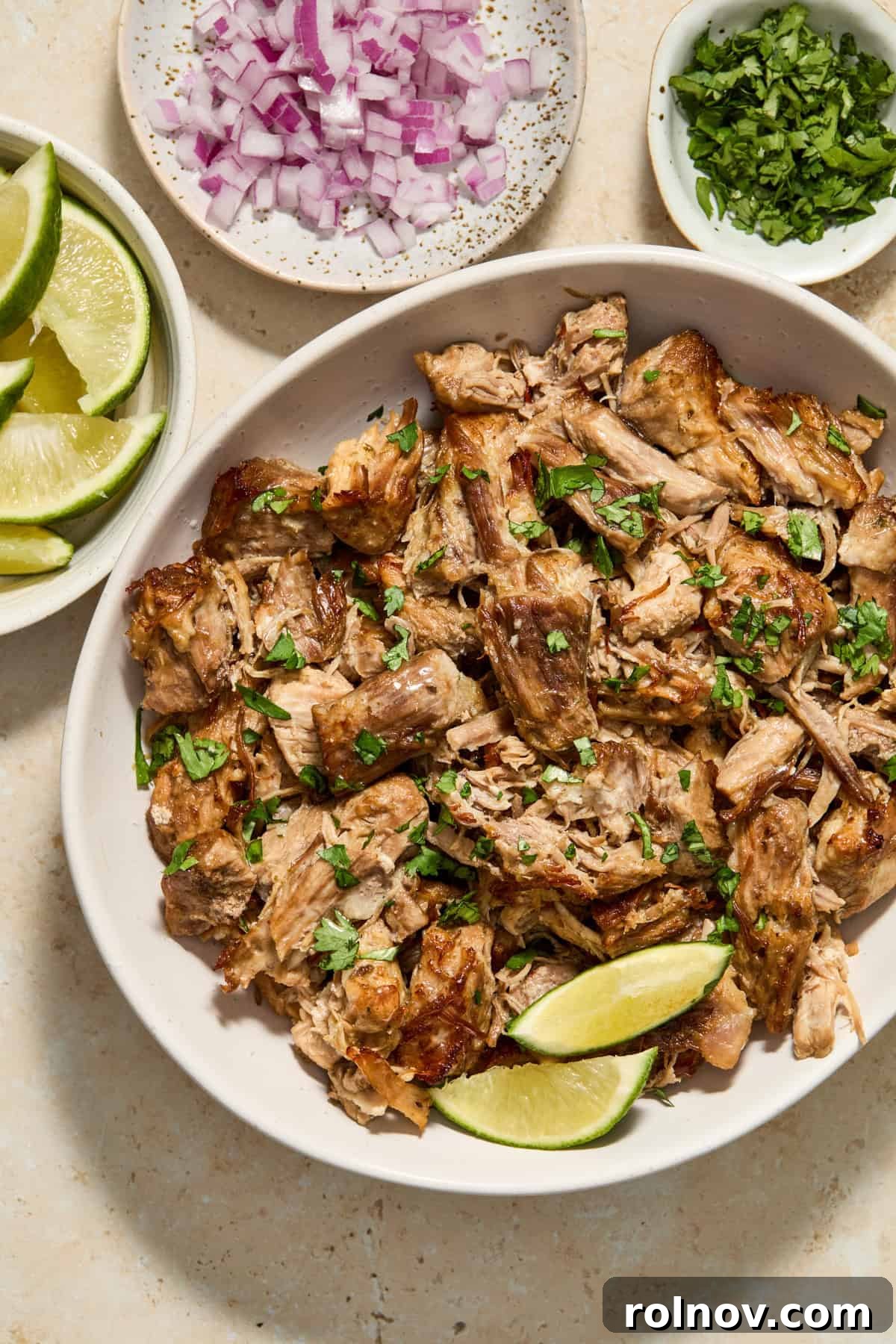 Lightning-Fast Crispy Instant Pot Carnitas 10 Bowl with shredded pork carnitas meat topped with cilantro and bowls of limes, onions and cilantro surrounding.