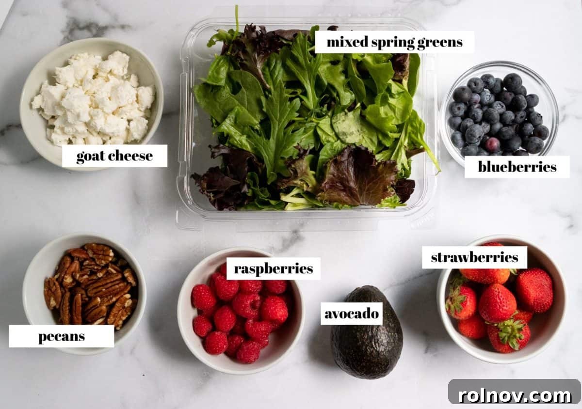 Strawberry Balsamic Berry Salad 3 Recipe ingredients for mixed green salad, labeled on a clean white countertop, featuring fresh berries, greens, goat cheese, pecans, and avocado.