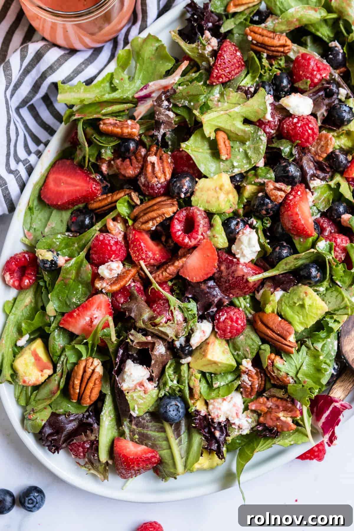 Strawberry Balsamic Berry Salad 7 Overhead view of a vibrant mixed green salad with an abundance of fresh berries, pecans, and goat cheese, invitingly presented on a white plate.