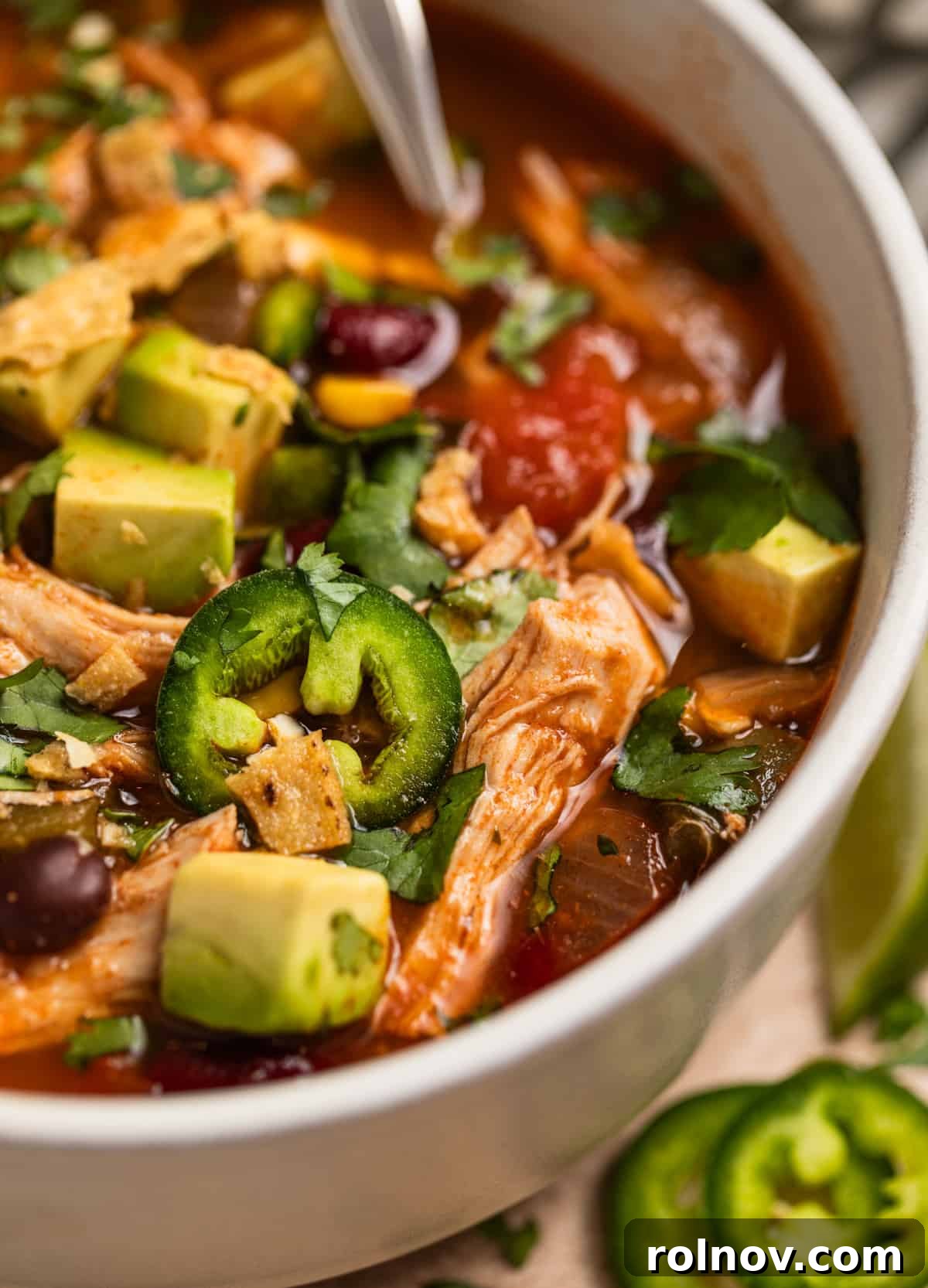 Ultimate Instant Pot Chicken Tortilla Soup 3 A close-up shot of a bowl of Instant Pot Chicken Tortilla Soup, with a spoon scooping into the rich, chunky texture filled with chicken, beans, corn, and vegetables, ready to be enjoyed.