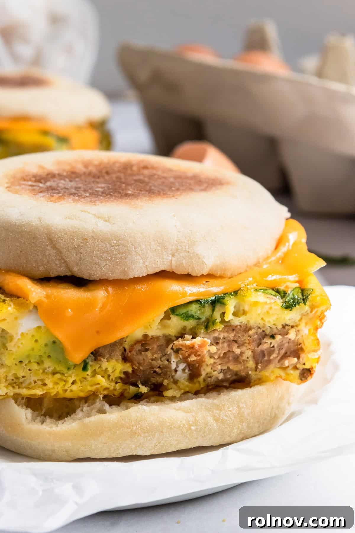 Delicious homemade sausage McMuffin with spinach and melted cheese, ready to eat.