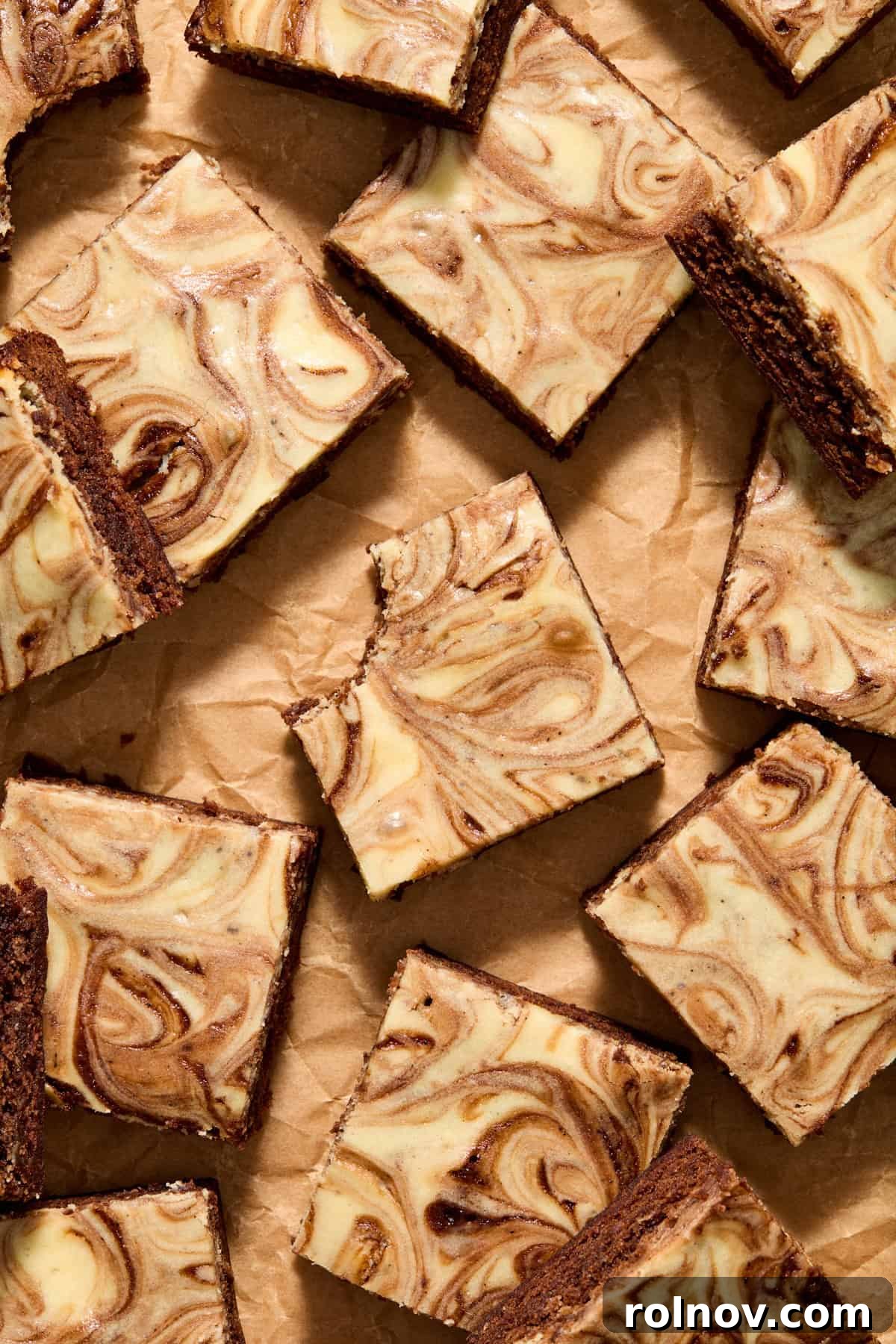 Kahlua Swirled Cream Cheese Brownie Bliss 2 Sliced Kahlua Cream Cheese Brownies arranged on parchment paper, showcasing their beautiful cheesecake swirls and rich chocolate texture. One brownie has a bite taken out, revealing its fudgy interior.