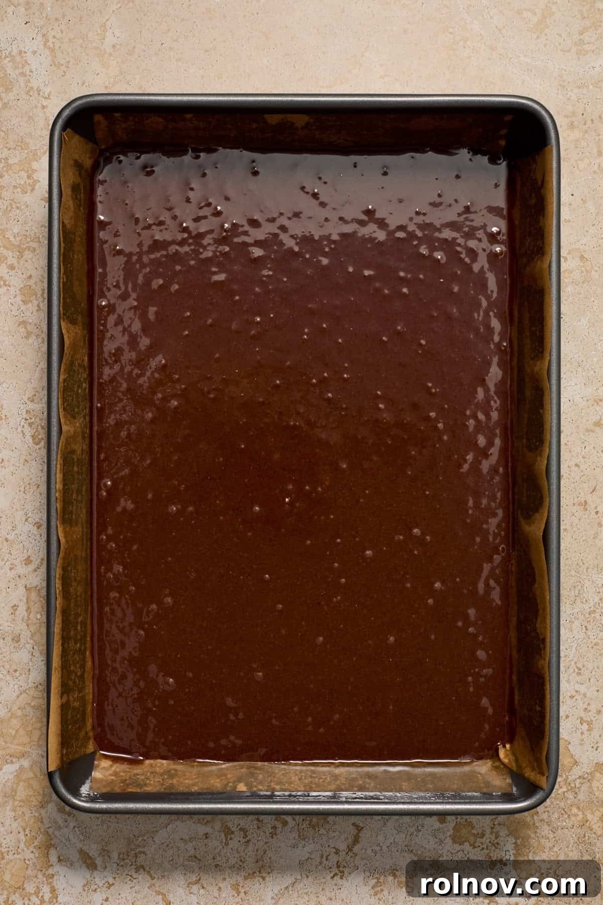 Kahlua Swirled Cream Cheese Brownie Bliss 5 Brownie batter spread evenly in a parchment-lined 9x13 inch baking pan, ready for the cheesecake swirl.