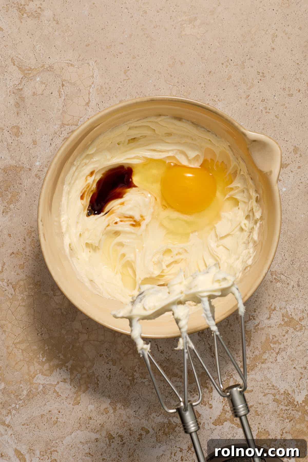 Kahlua Swirled Cream Cheese Brownie Bliss 6 A room temperature egg and vanilla extract being added to a bowl of creamed sugar and softened cream cheese.