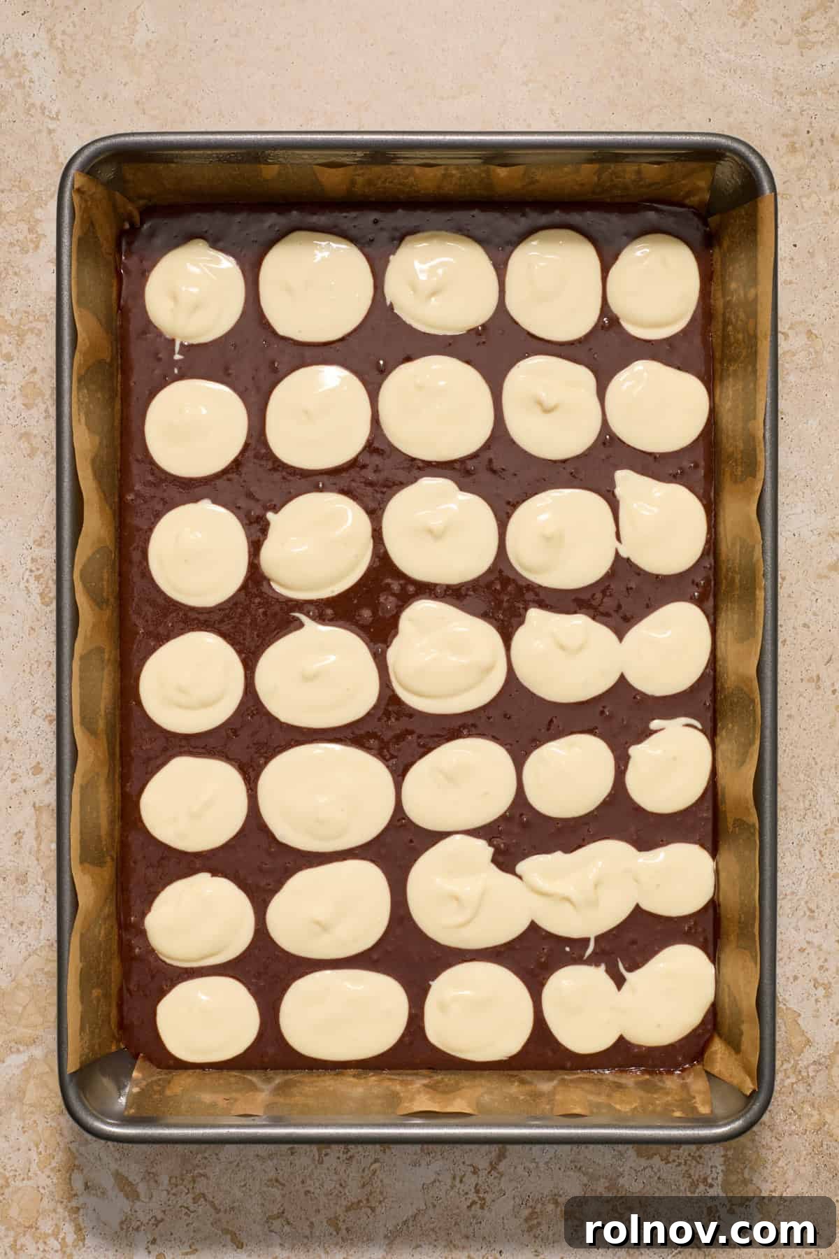 Kahlua Swirled Cream Cheese Brownie Bliss 8 Dollops of white cream cheese mixture evenly distributed over the dark brownie batter in a baking pan, prior to swirling.