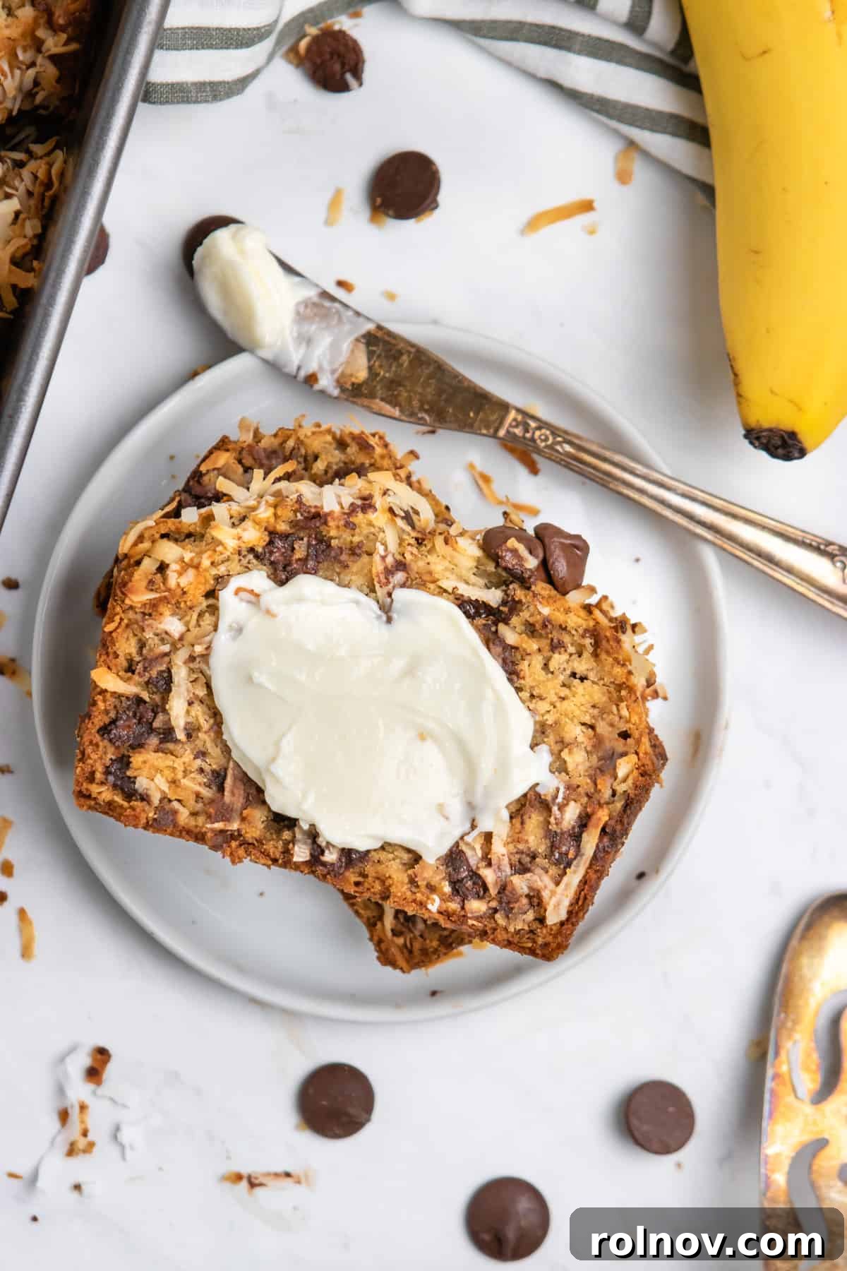 Overhead view of a freshly baked loaf of coconut banana bread with butter melting on top, garnished with toasted coconut flakes.