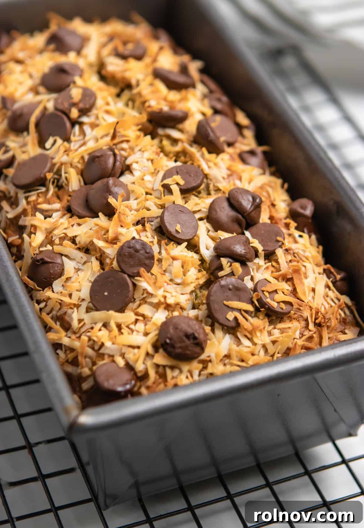 A freshly baked loaf of coconut banana bread resting on a cooling rack, showcasing its golden-brown crust and toasted coconut topping.