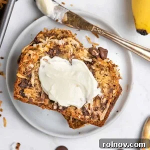 Coconut chip banana bread on white plate with butter spread on top.
