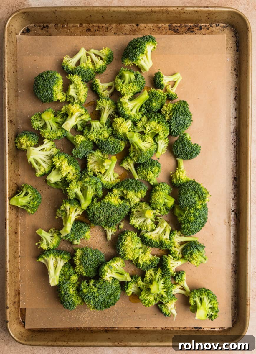 Sticky Orange Chicken One-Pan Dinner 7 Broccoli on parchment lined baking sheet tossed in olive oil and seasoning.
