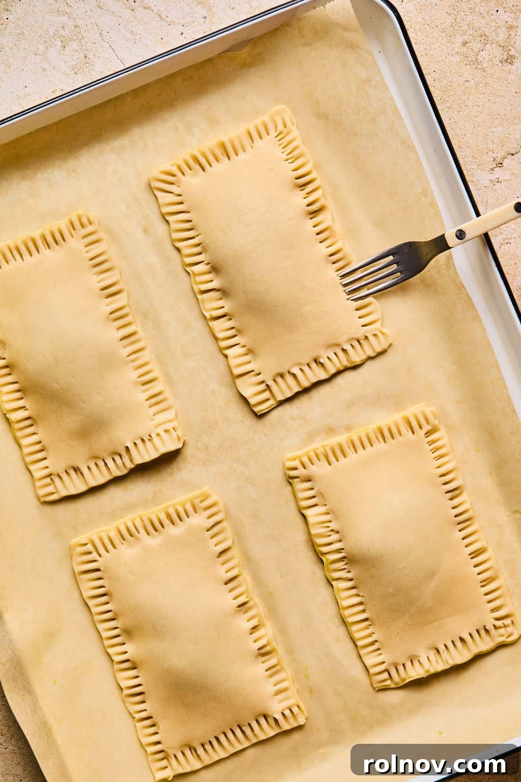 A fork is used to further crimp and seal the edges of a homemade pop tart, adding a decorative pattern before baking.