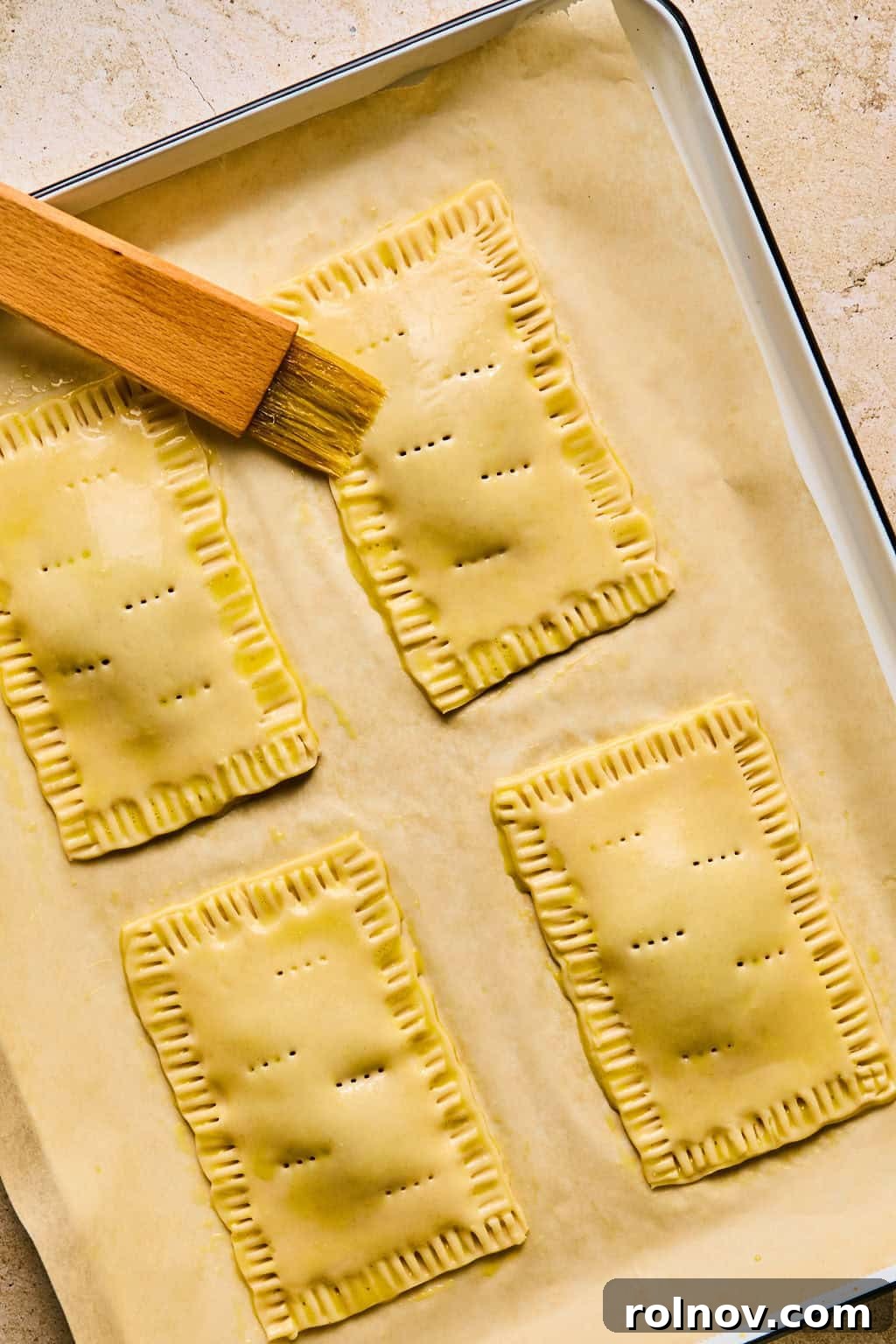 A pastry brush applies egg wash to the top and edges of a homemade pop tart, preparing it for a golden bake.