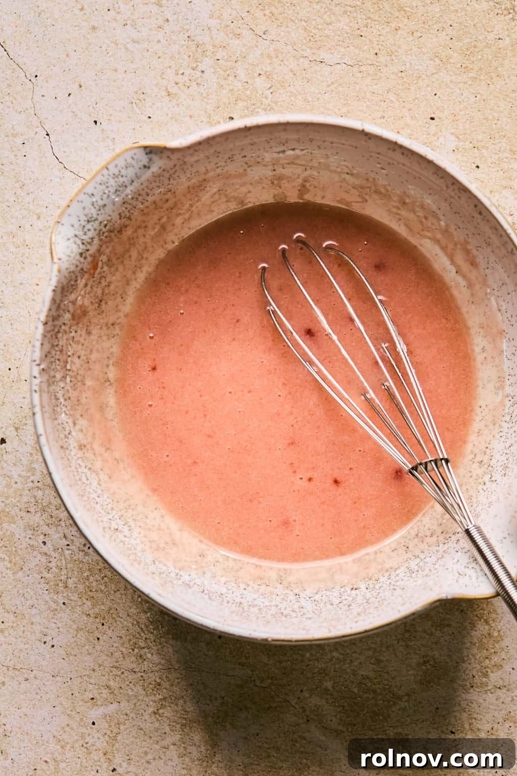 Smooth, pink strawberry icing freshly whisked in a mixing bowl, ready for application.