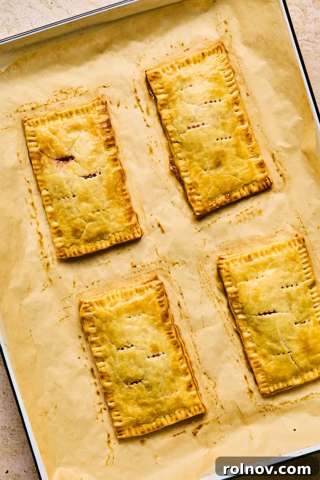 A tray of perfectly baked homemade pop tarts, golden brown and un-iced, cooling on parchment paper.
