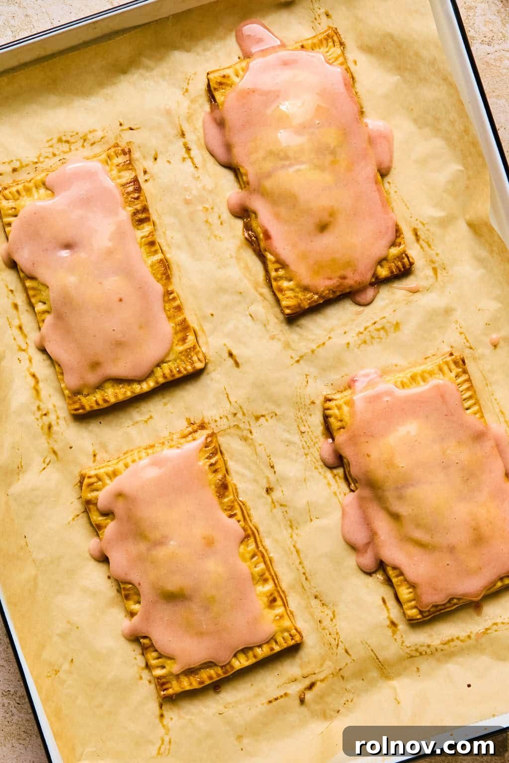 Fully iced homemade pop tarts adorned with colorful sprinkles, resting on parchment paper after baking.