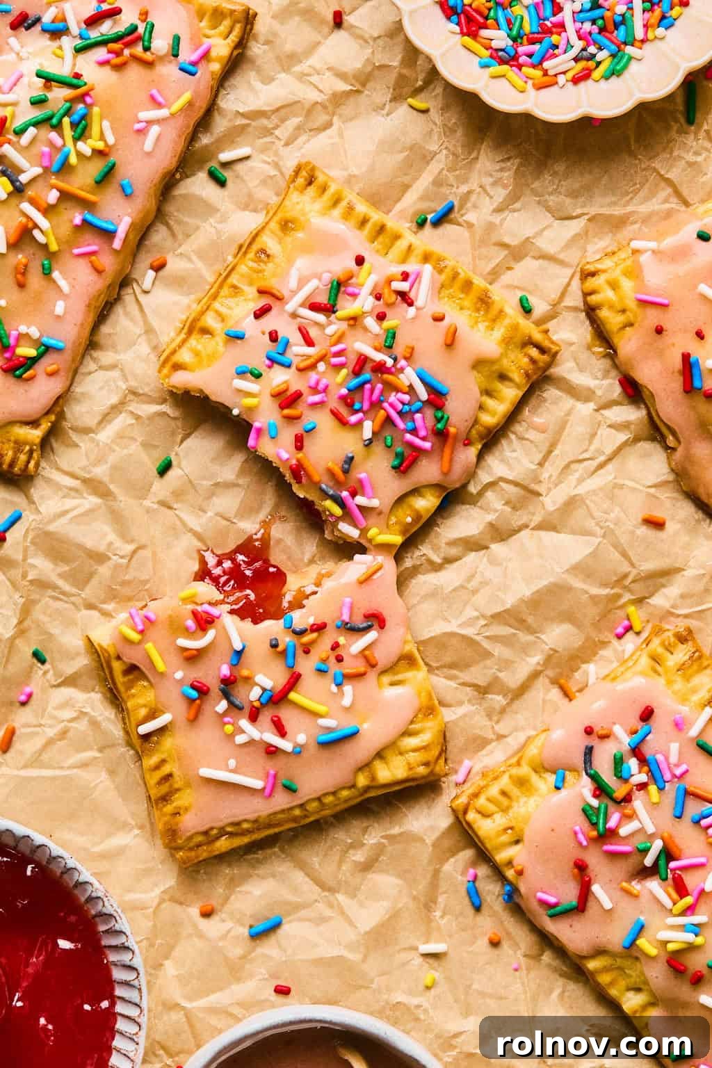Overhead view of several breakfast pastries, perfectly baked and adorned with colorful sprinkles, arranged on brown parchment paper.