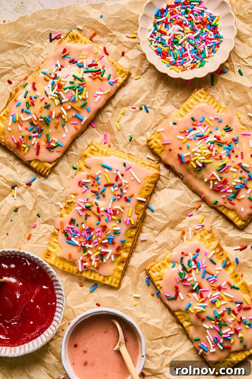 An assortment of colorful homemade pop tarts arranged on parchment paper, each topped with vibrant rainbow sprinkles.
