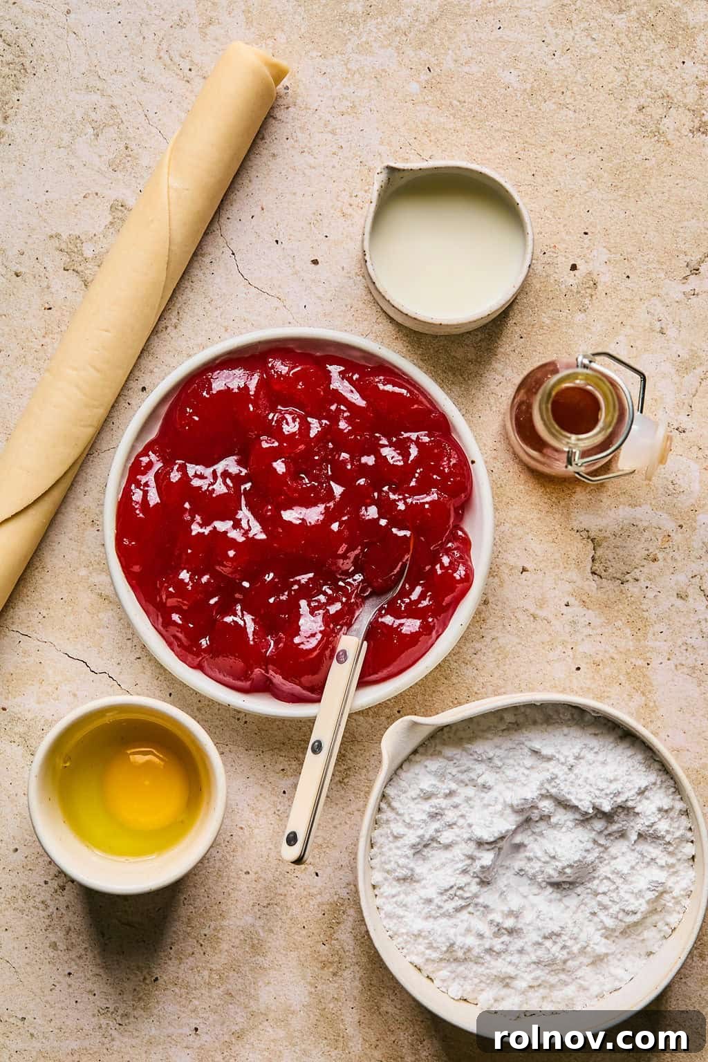 Ingredients for homemade pop tarts, including pie crust, various jams, eggs, and icing components, neatly arranged on a light surface.