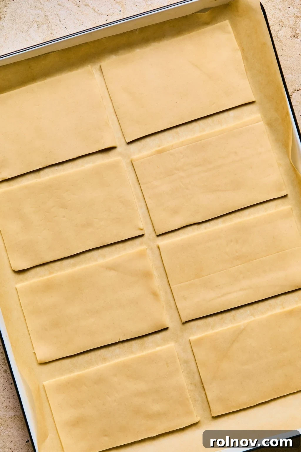 Parchment paper-lined baking sheet showcasing neatly cut rectangular pieces of pie crust, ready for filling.