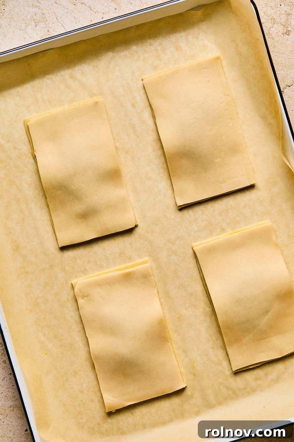 The top layer of pie crust being carefully placed over a jam-filled bottom layer on a baking sheet, forming the complete pop tart.