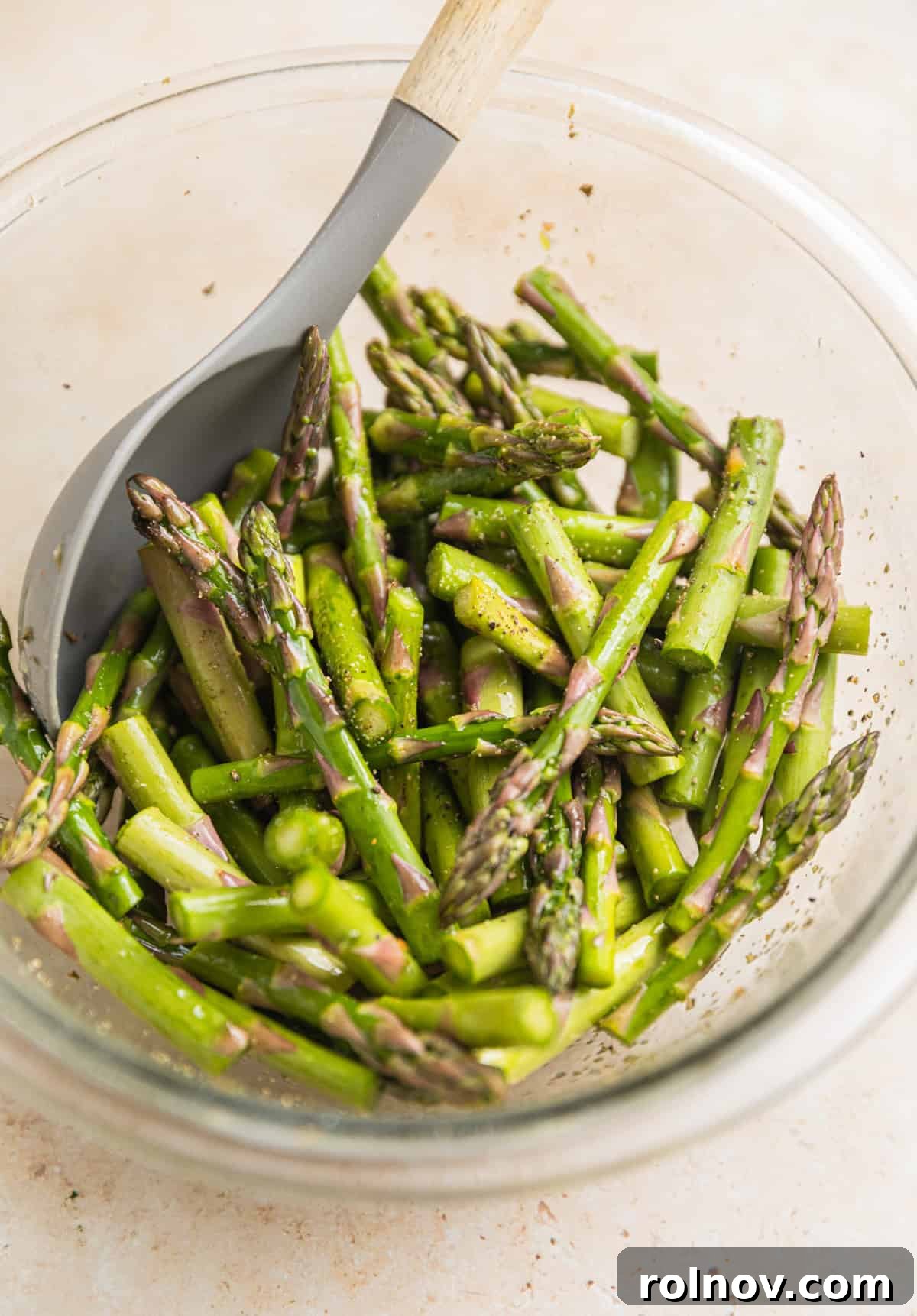 Verdant Burrata Delight 5 Fresh asparagus pieces seasoned and ready in a bowl with a spoon, awaiting roasting.