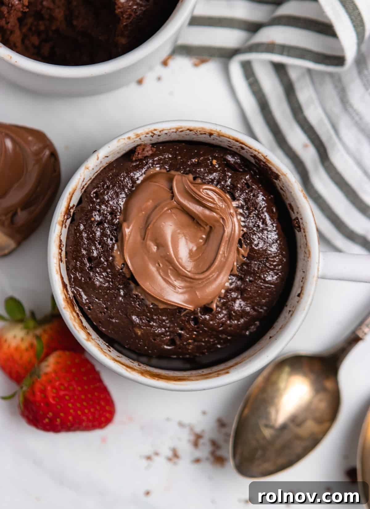 5-Minute Nutella Mug Cake 2 Overhead view of Nutella chocolate cake in mug with strawberries and spoon.