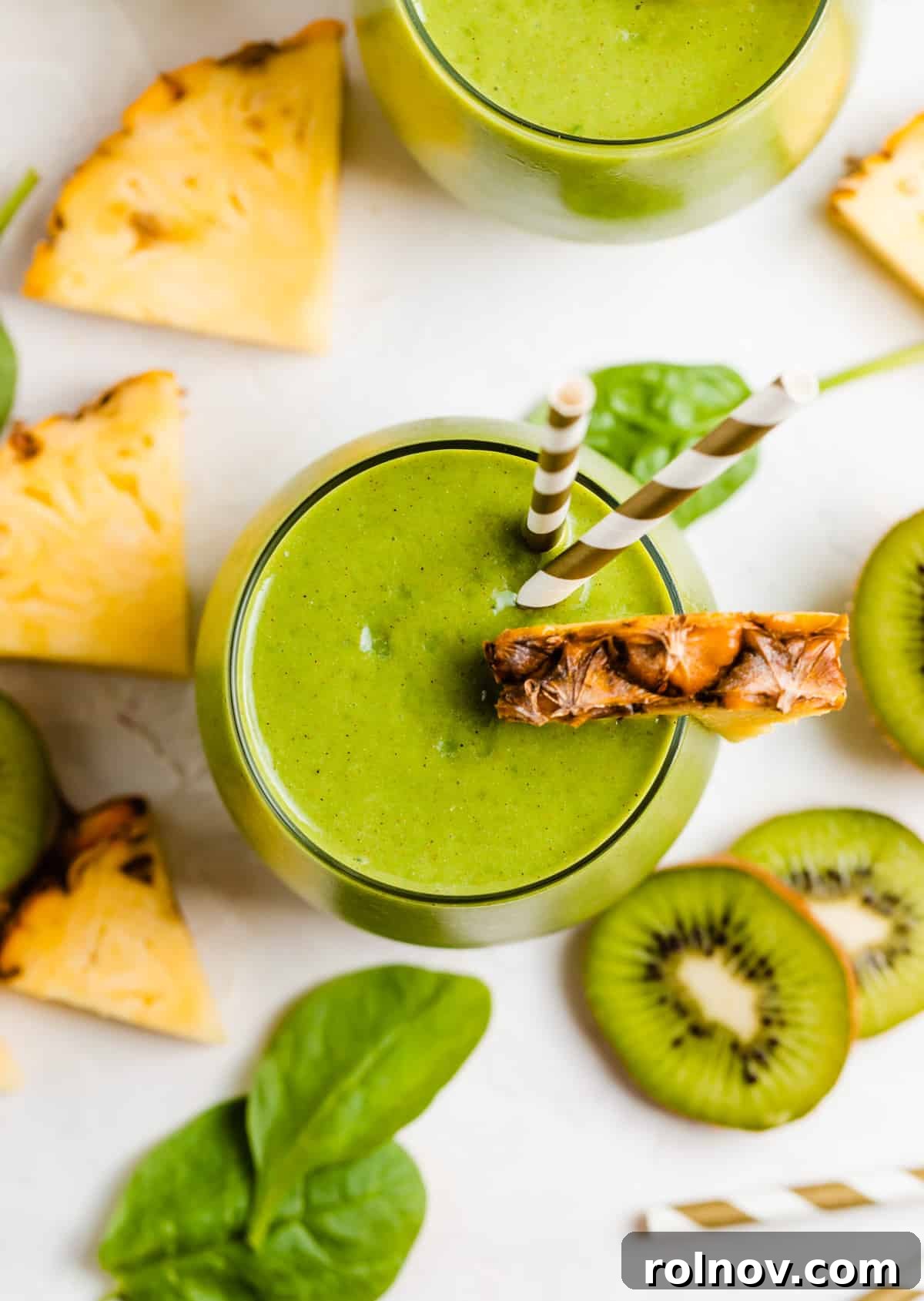 Zesty Green Kiwi Pineapple Boost 5 Green kiwi pineapple smoothie in glass with pineapple and kiwi slices surrounding.