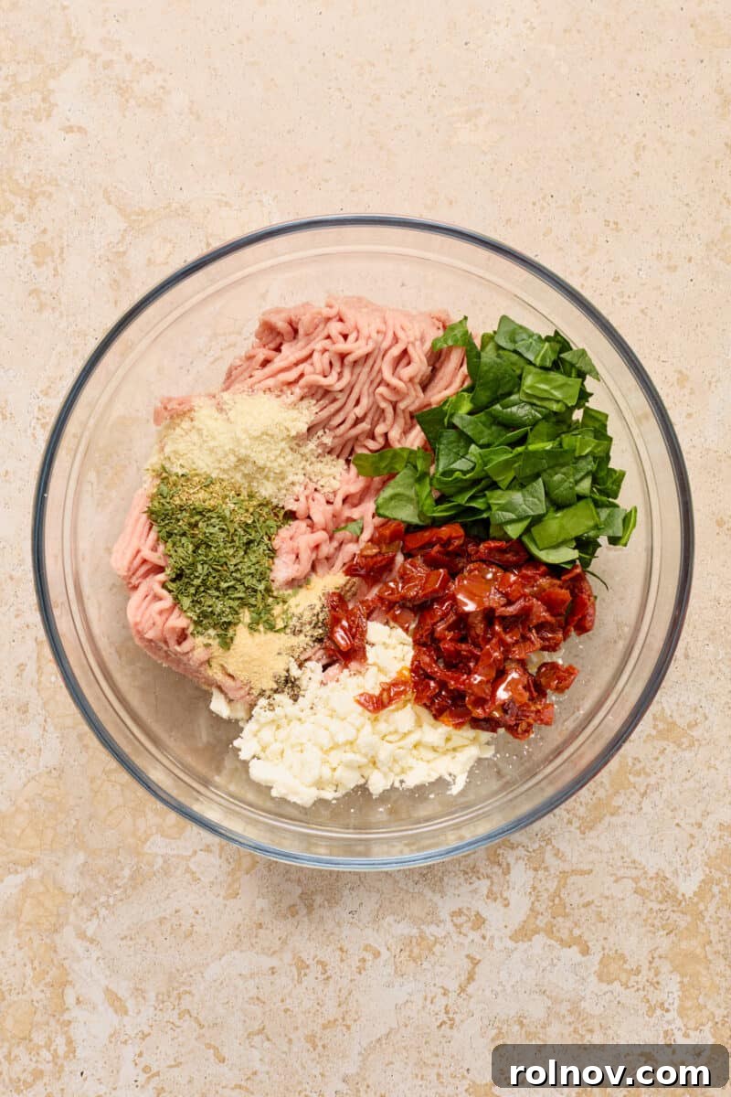 Ground turkey, spinach, feta, seasoning and other ingredients to make turkey burgers in glass bowl.