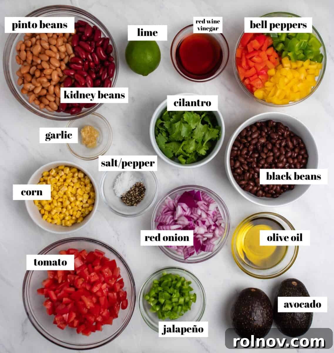 Various prepped ingredients for the 3 Bean Avocado Corn Salad laid out on a kitchen counter, including chopped bell peppers, rinsed beans, fresh cilantro, ripe avocado, and sweet corn, labeled for clarity.