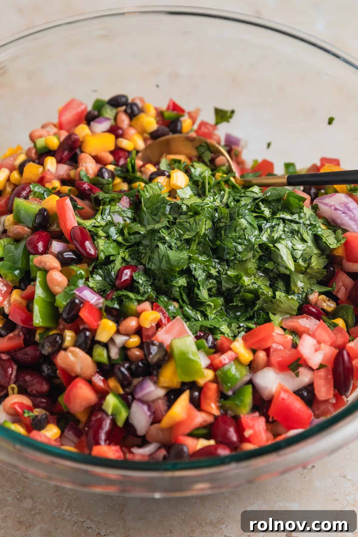 Freshly chopped cilantro being added to a mixing bowl, already filled with the prepped bean and corn salad ingredients, enhancing its fresh aroma and color.