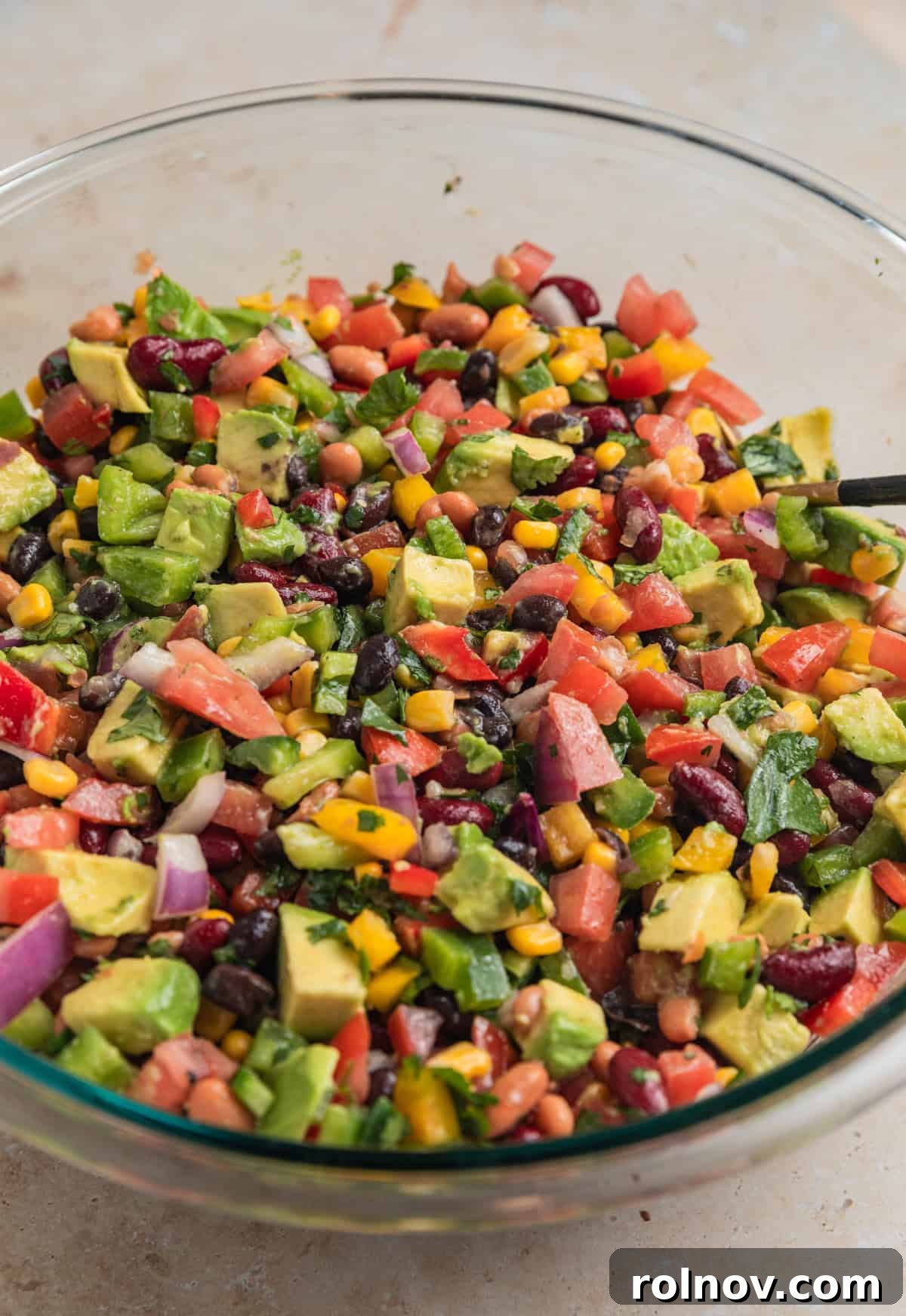The fully mixed 3 Bean Avocado Corn Salad in a mixing bowl, featuring cubed avocado gently incorporated with the beans, corn, and other vegetables, ready for chilling.
