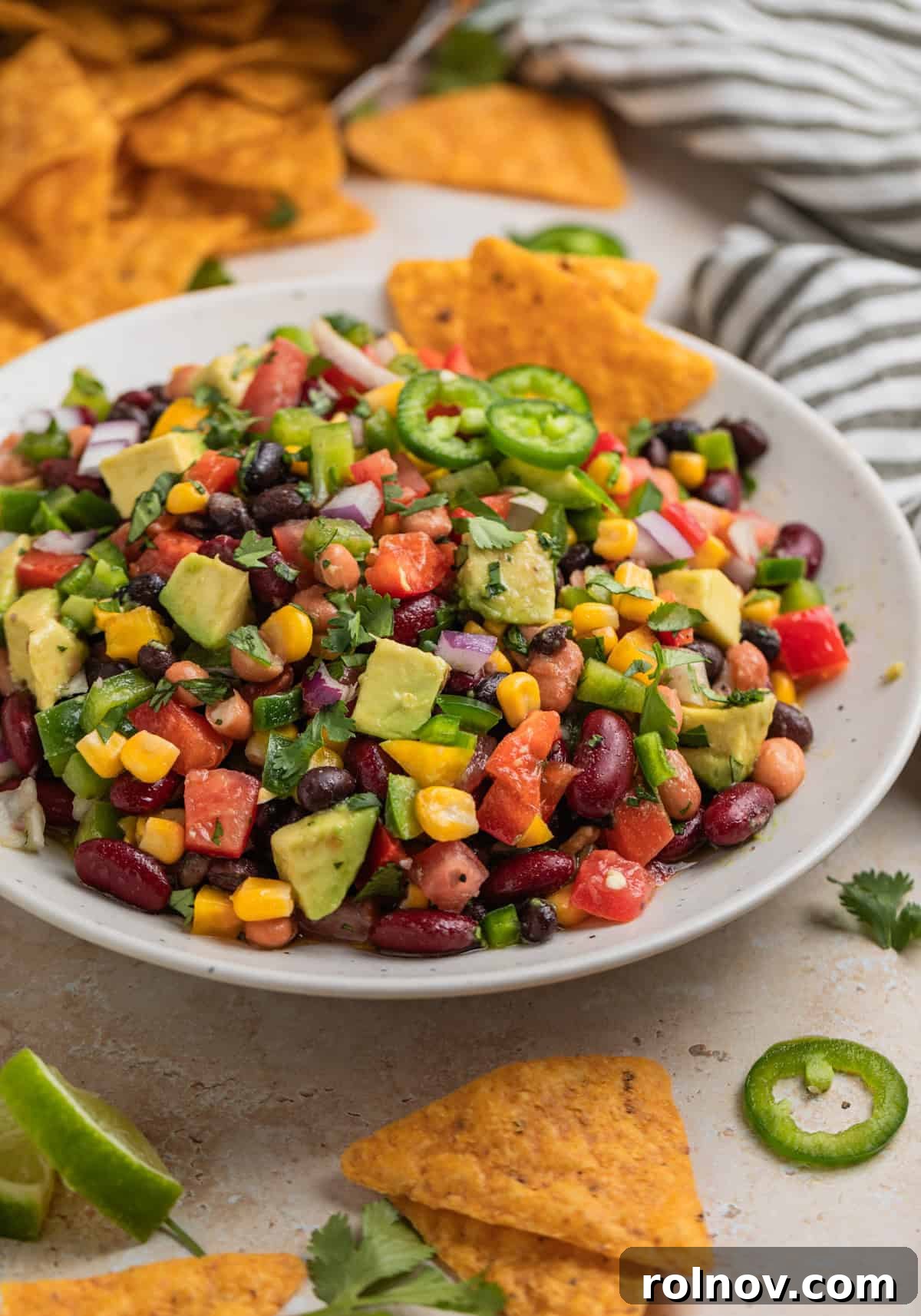 Crispy tortilla chips being dipped into a luscious 3 Bean Avocado Corn Salad, showcasing its vibrant blend of corn, beans, avocado, and fresh cilantro, ready to be enjoyed.