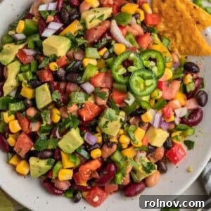 Tortilla chips dipping into a bowl filled with kidney beans, black and pinto beans, fresh vegetables, creamy avocado, and sweet corn.