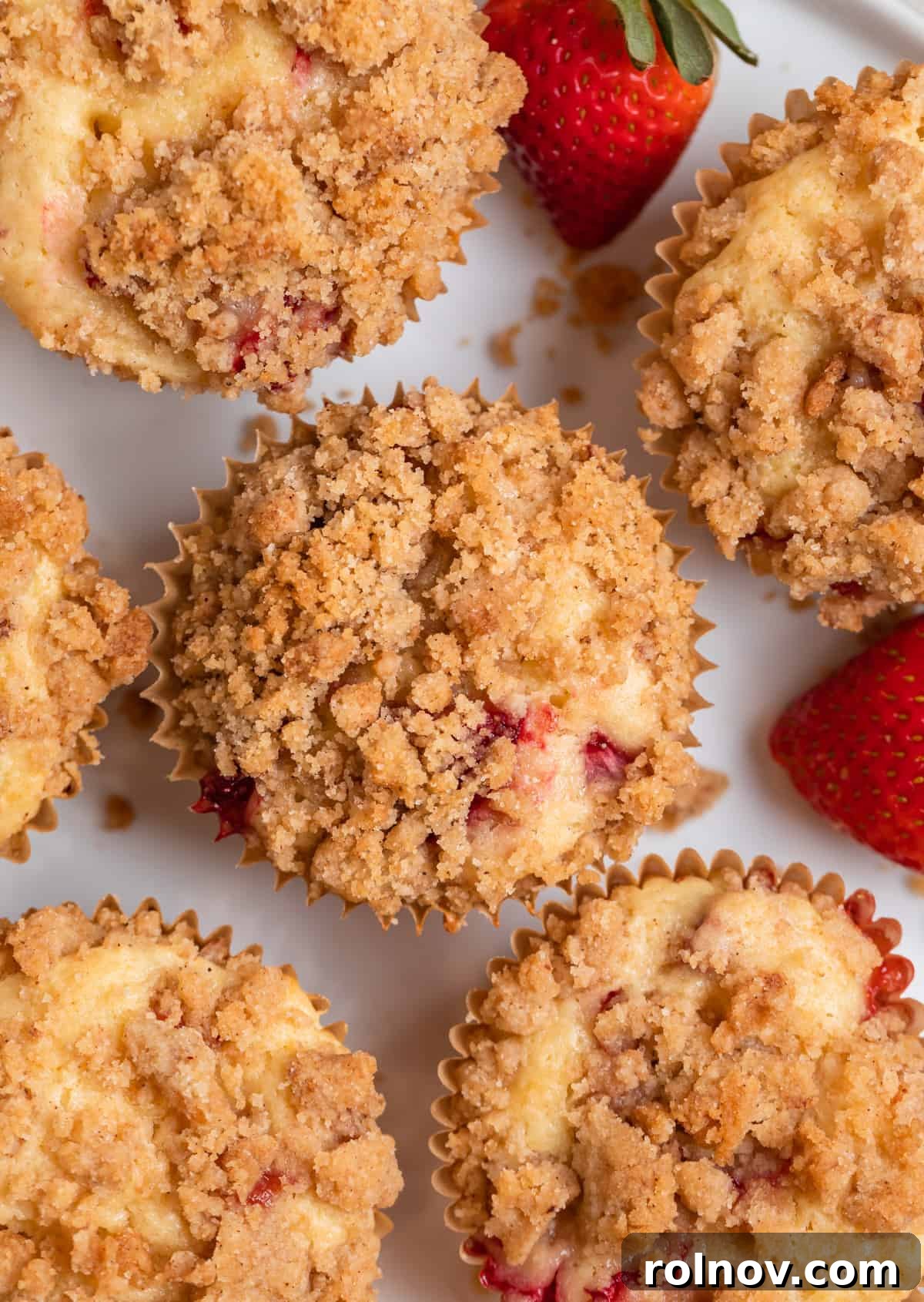 Sweet Strawberry Crumble Muffins 9 Finished strawberry muffins with streusel topping arranged on a plate with fresh berries and scattered crumbs.