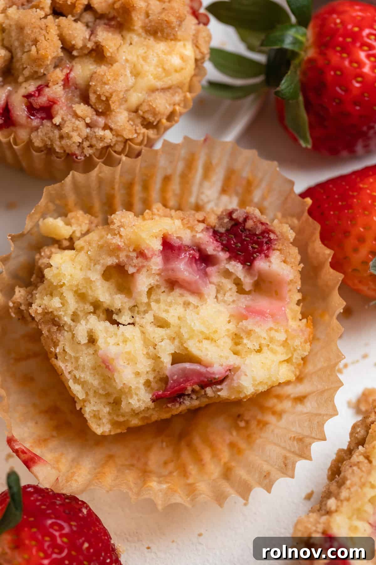Sweet Strawberry Crumble Muffins 10 A halved strawberry crumb muffin resting in a muffin cup, surrounded by fresh berries.