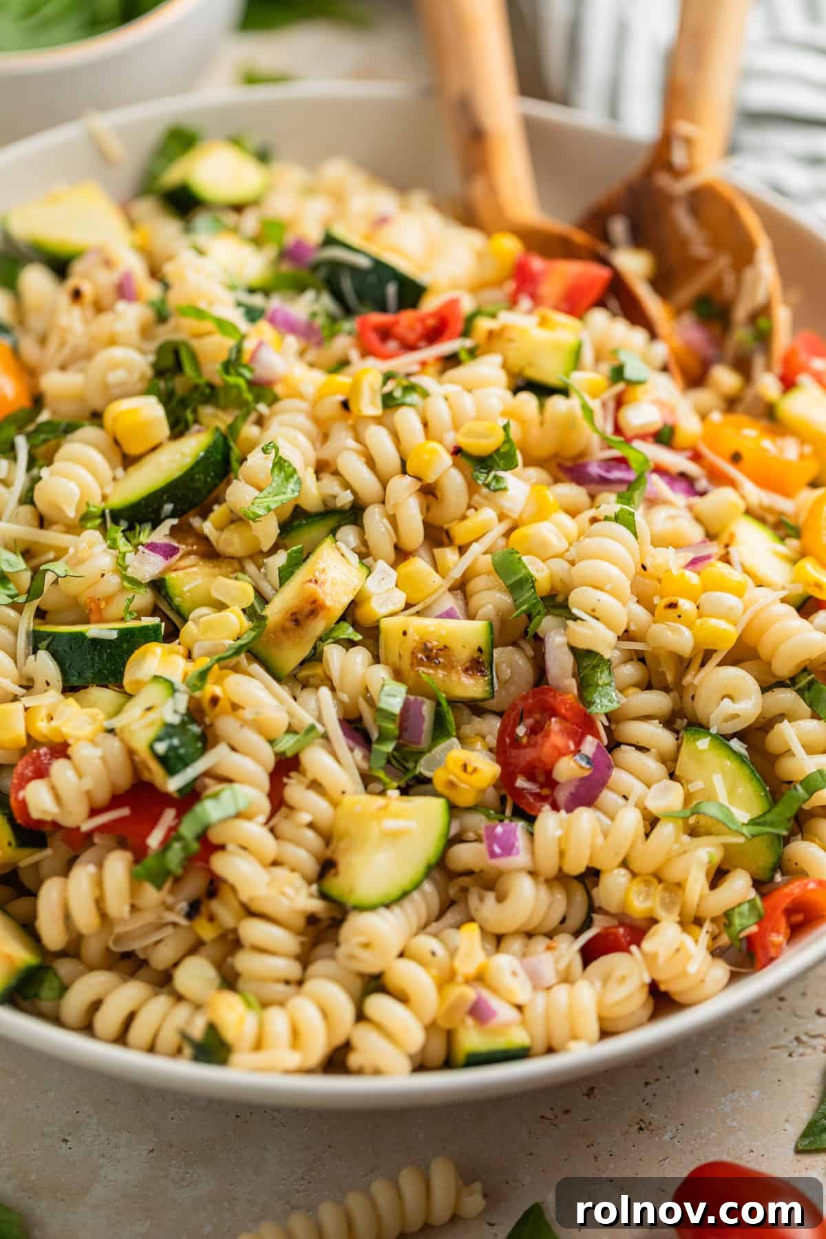 Charred Zucchini Pasta Toss 2 A large bowl of grilled zucchini pasta salad, featuring spiral pasta, charred corn kernels, bright red cherry tomatoes, and fresh basil leaves, garnished with grated Parmesan cheese.